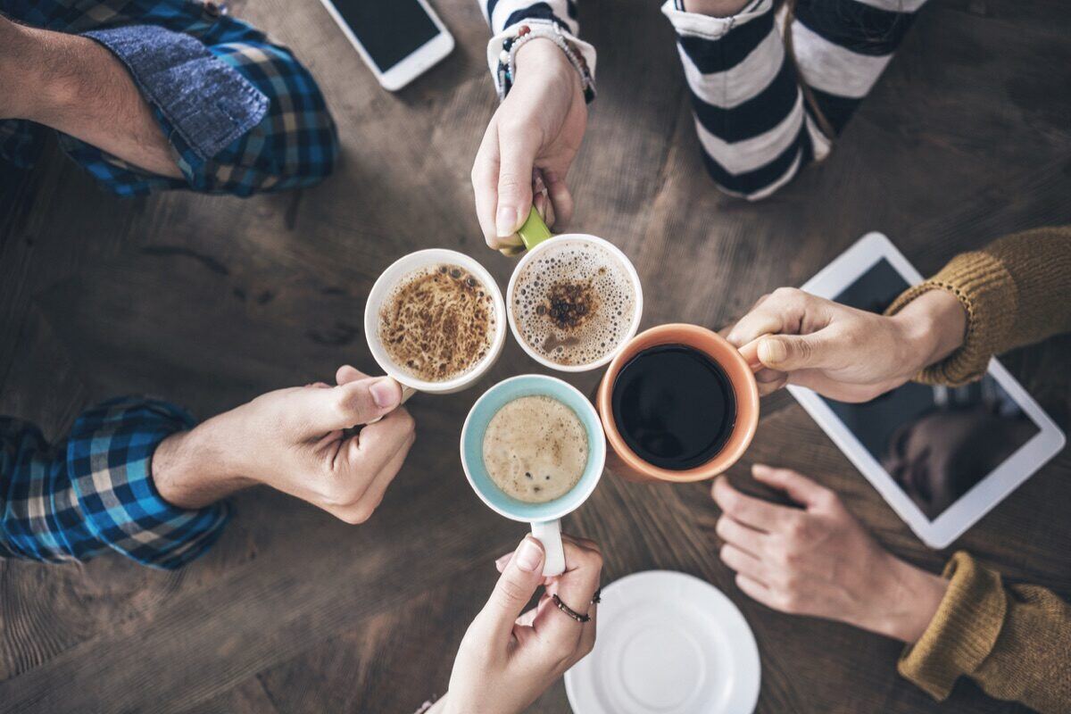 Six people cheers with coffee cups around a wooden table