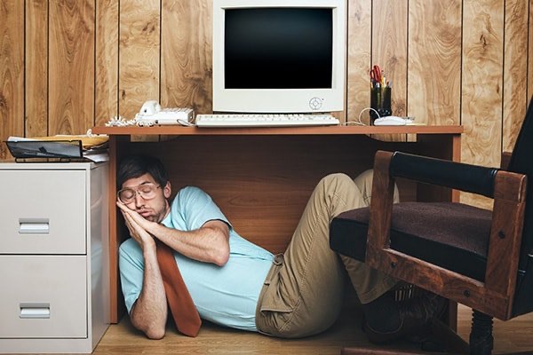 Employee asleep under his desk with a computer on top of it